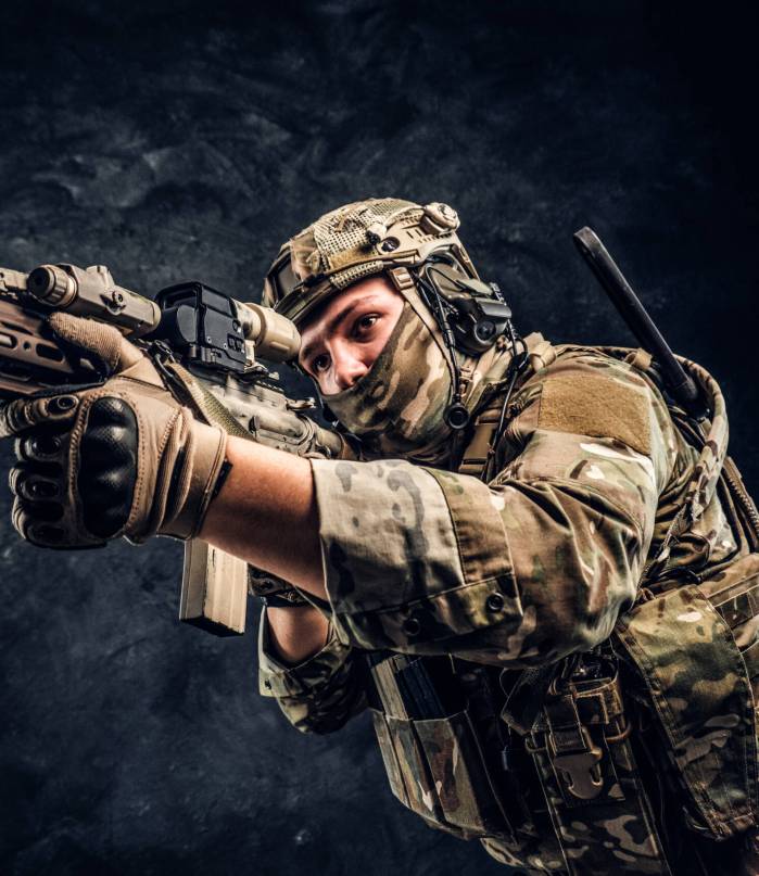 Fully equipped soldier in camouflage uniform holding an assault rifle Private security service contractors, the elite special unit, full protective soldier holding assault rifle aiming at the target. Studio photo against a dark wall.